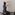 A person in a black west and trousers is kneeling in front of a plain wall and writing on a piece of paper rested on the wall. Other sheets of paper are scattered on the floor, and an open laptop on the right. The setting is minimalistic, with neutral colours.