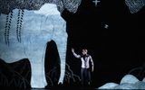 A person stands next to a large, white, illustrated elephant and trees on a dark stage, reaching out toward the animal.