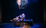 Marc Brew/Sidi Labi - an Accident/ a Life © FilipVanRoe_Eastman company Marc Brew by Sidi Larbi Cherkaoui A man sits on a box. Above him is a car, suspended from the ceiling. A person lies across his knees, their head on his arm.