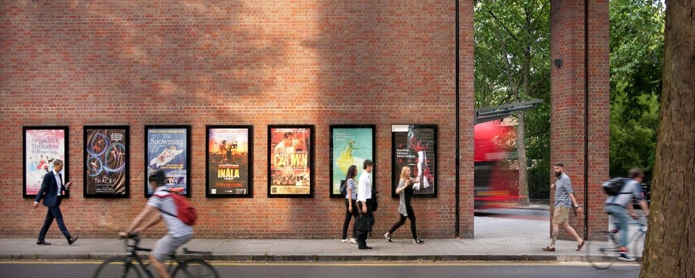 SWT front side A photo of the outside wall of Sadler's Wells Theatre building with show posters and pedestrians and a cyclist passing by