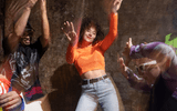 Candoco Over and Over © Hugo Glendinning A blurry image of five people in bright clothes dancing against a rocky background. There is a feeling of joy.